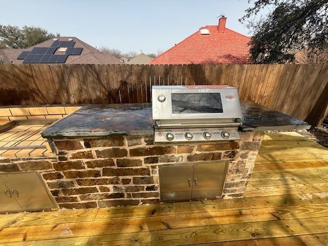 Outdoor brick barbecue grill with metal lid and stove top in a backyard patio.