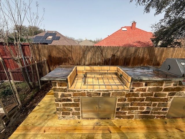 Outdoor brick barbecue pit with metal grill grate in a fenced backyard