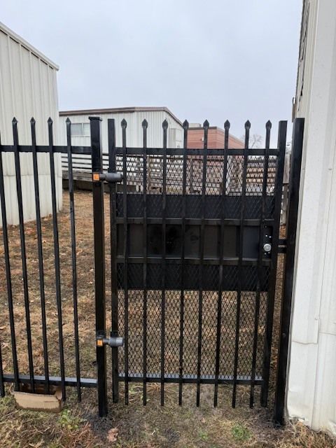 Black metal gate with vertical bars between white walls in a narrow outdoor passageway.