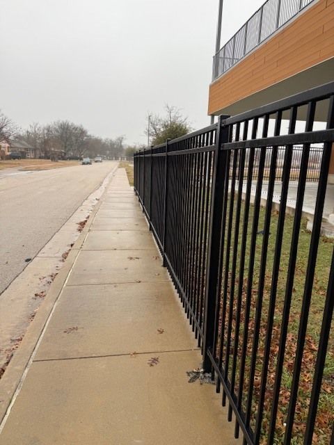 Sidewalk beside a black metal fence and brick building on an overcast street