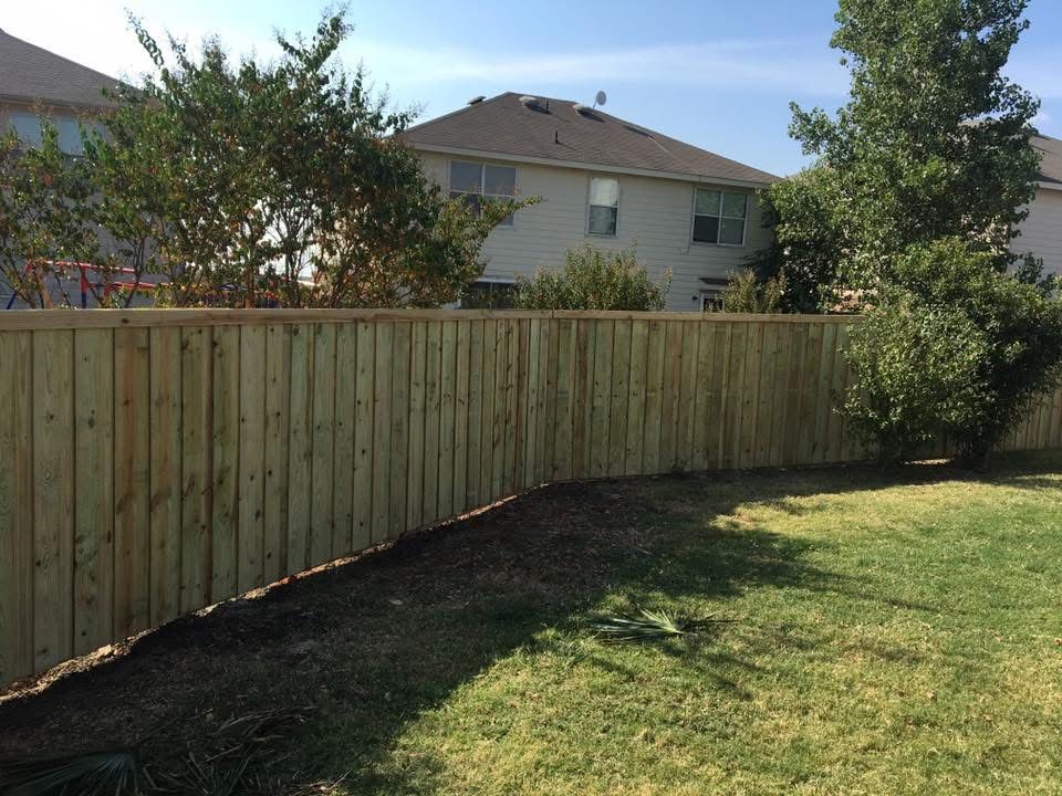 Wooden backyard fence along a grassy lawn with trees and a house in the background