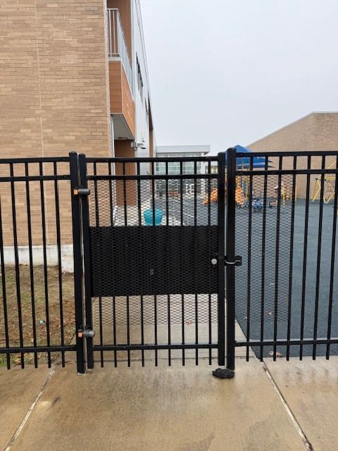 Black metal gate across a walkway between brick buildings, with a blue object behind it.