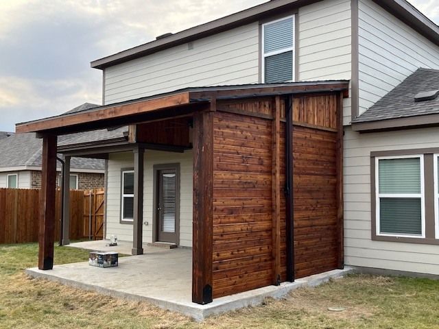 Wood-paneled covered patio addition on a suburban house with a concrete slab and wooden posts