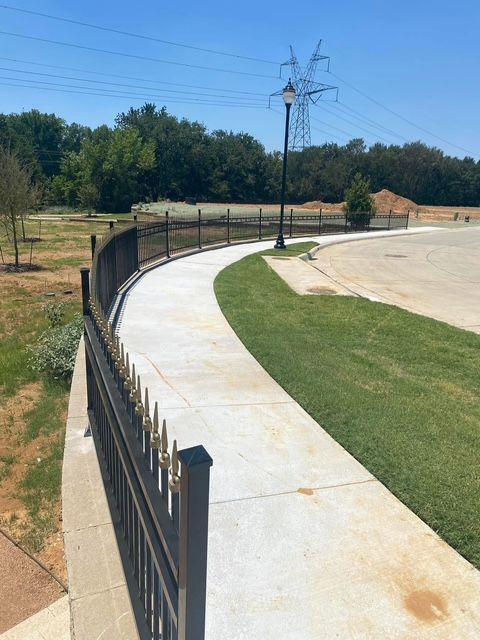 Curving concrete walkway beside black fence and green grass in a sunny park