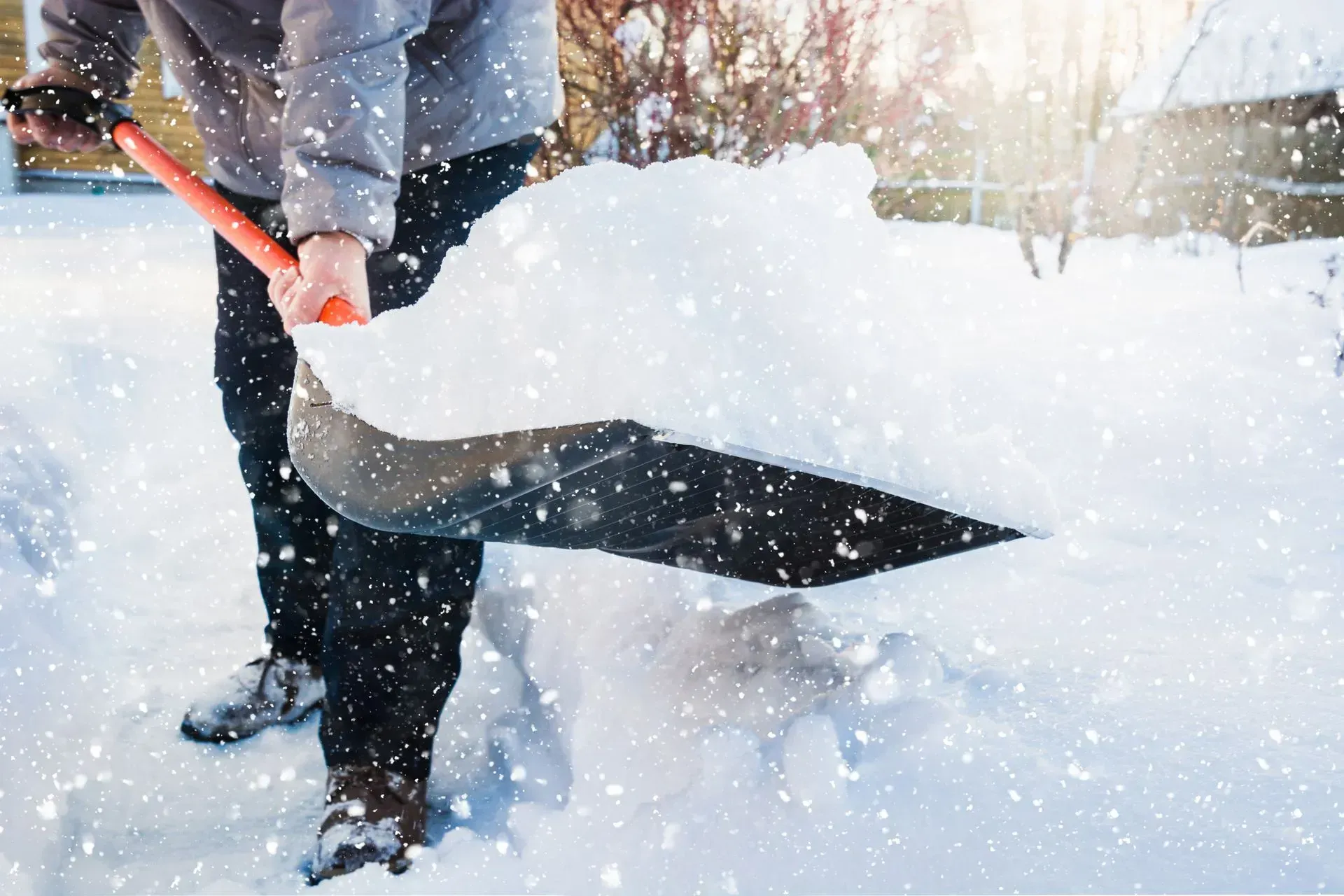 Person shoveling snow with a red shovel in a snowy outdoor scene
