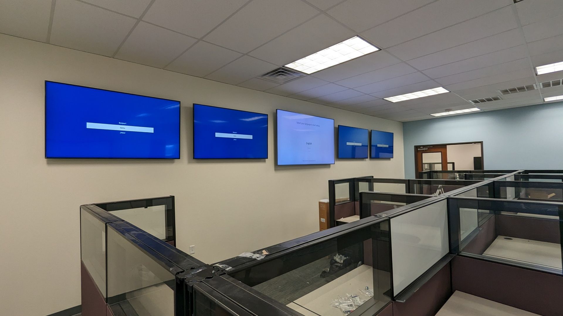 A room with cubicles and a row of monitors on the wall.