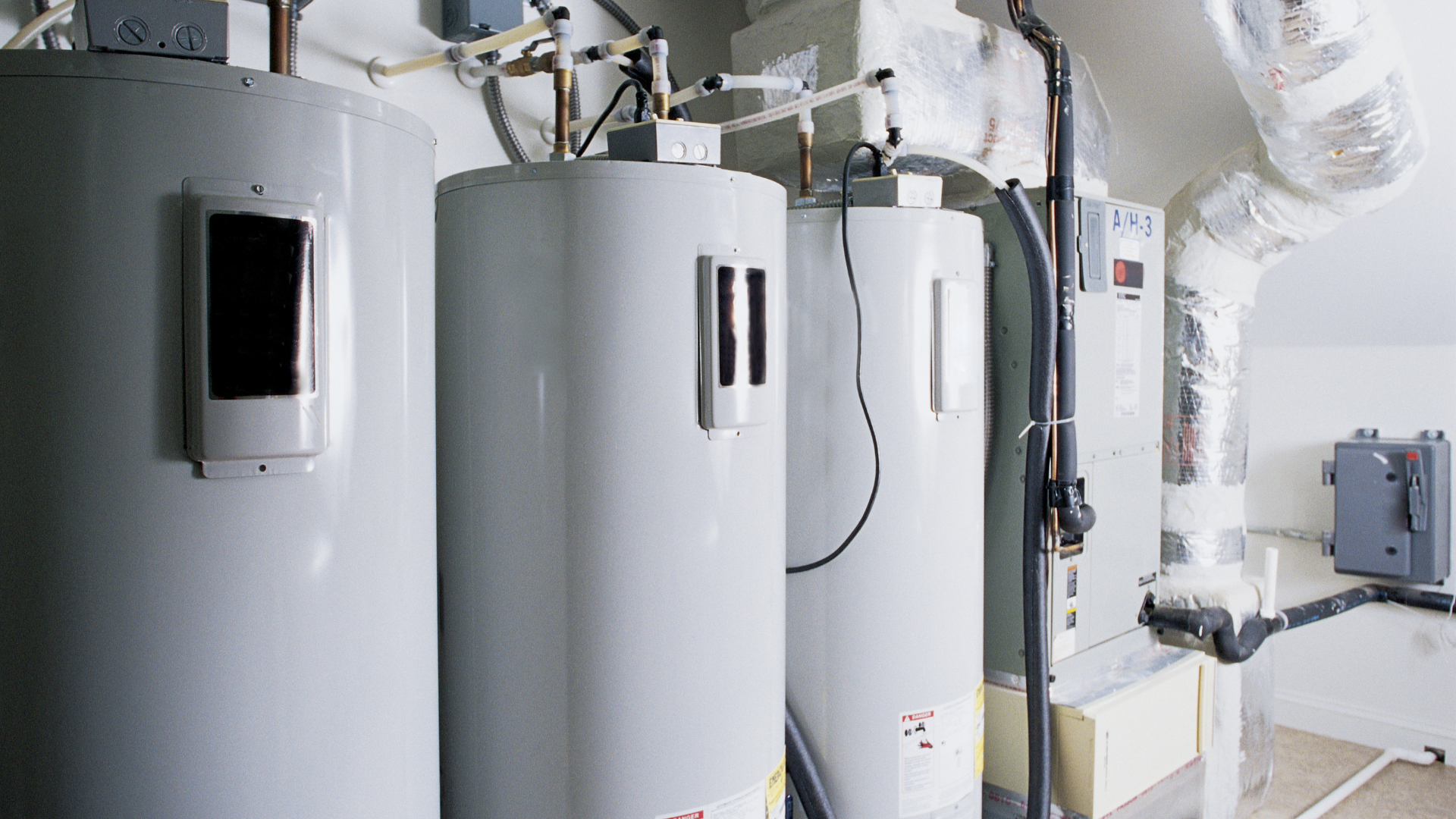 Three water heaters are sitting next to each other in a room.