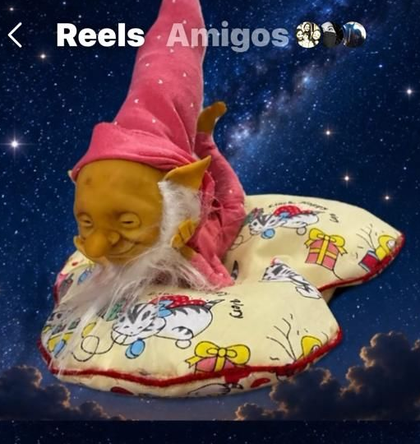 Muñeca vestida de rosa tumbada boca abajo en una estantería, con las piernas levantadas, y otras muñecas al fondo.