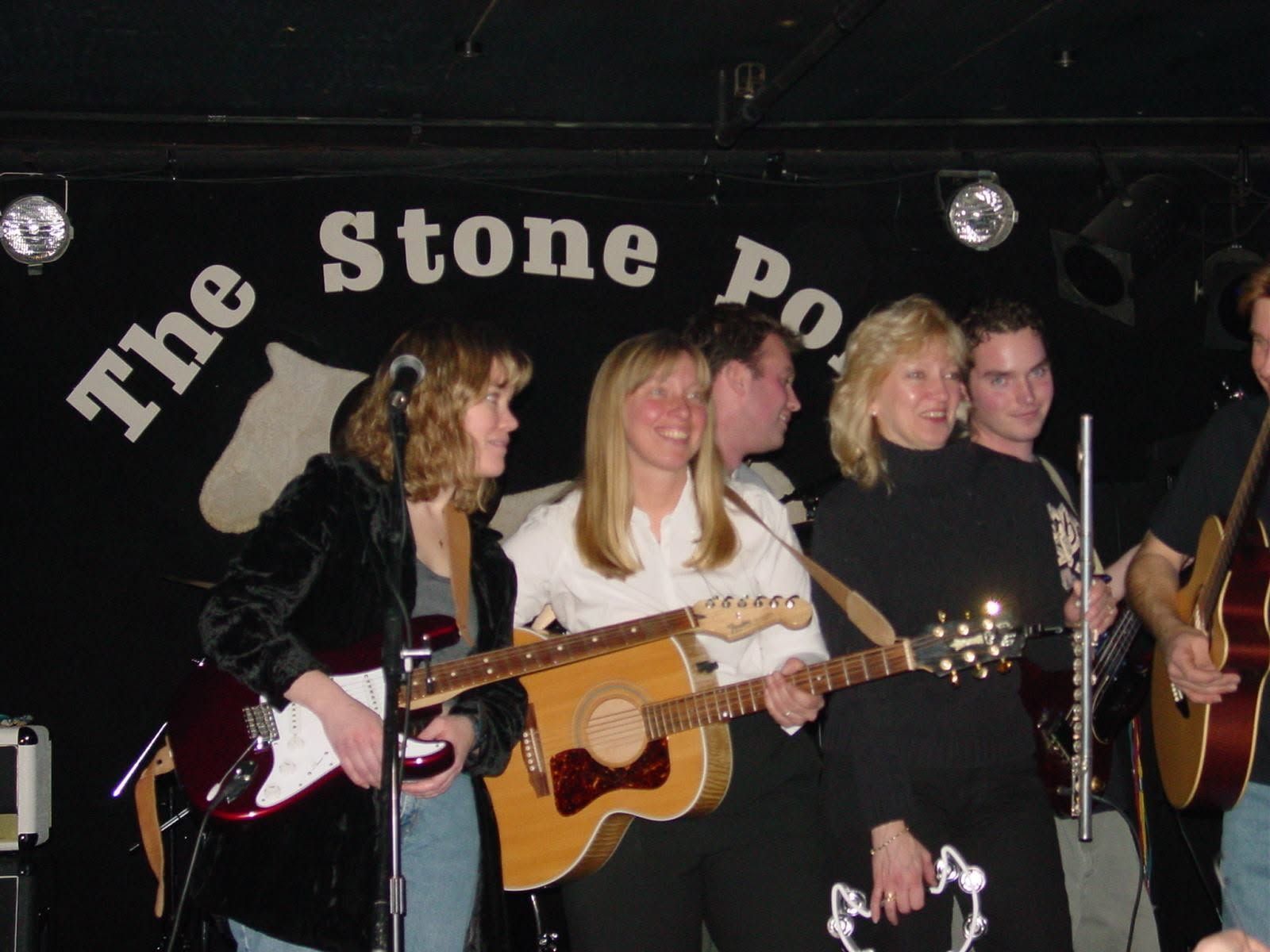 Four musicians performing onstage at The Stone Pony, holding guitars and microphones under dim lights