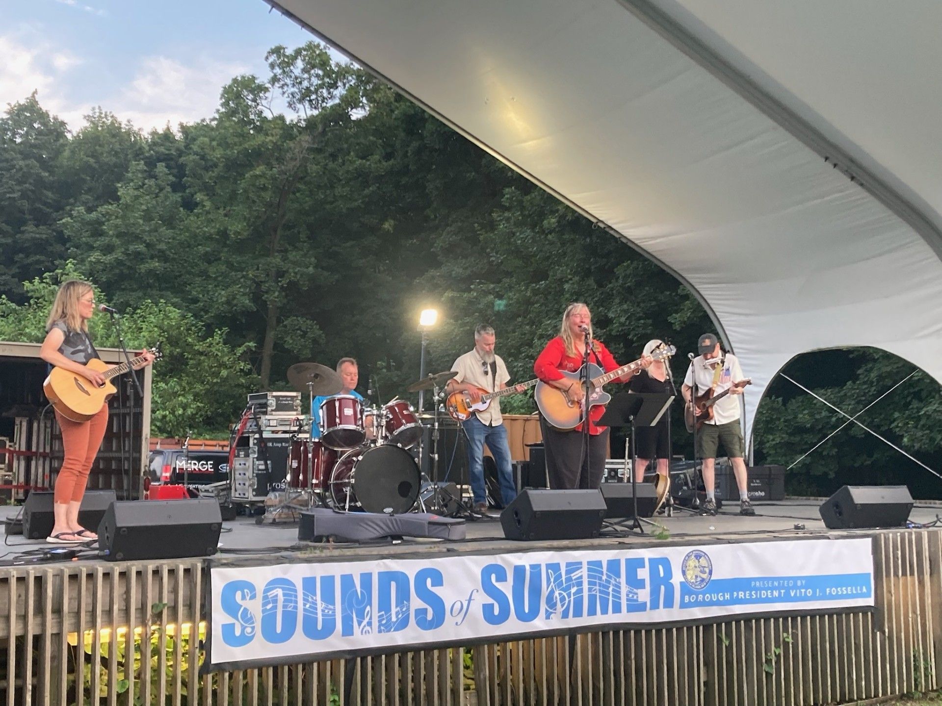Band performing on an outdoor stage under a tent at Sounds of Summer event