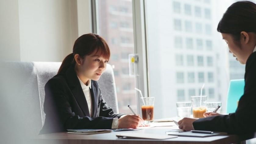 Two coworkers in a bright office meeting over documents, with drinks on the table.