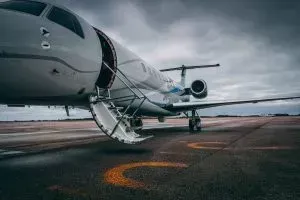 A private jet with an open door, parked on a runway under a cloudy sky.