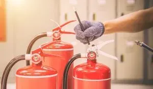 Person inspecting fire extinguishers. Red tanks, gloved hand, indoor setting.