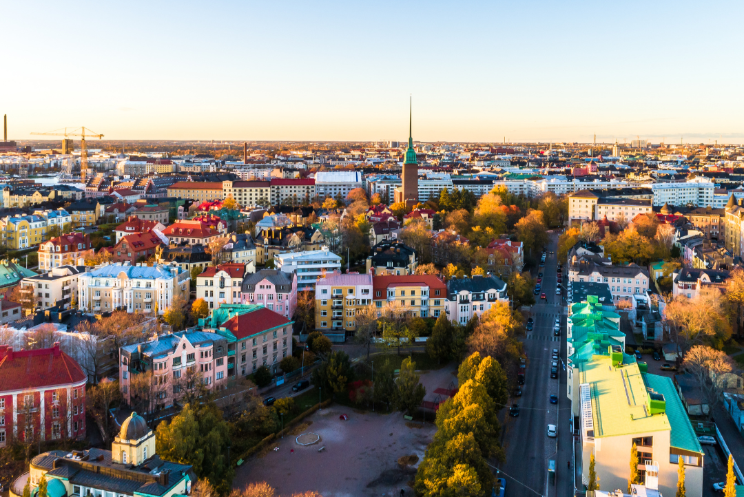 Aerial view of a colorful city neighborhood at sunset with streets, trees, and low-rise buildings.