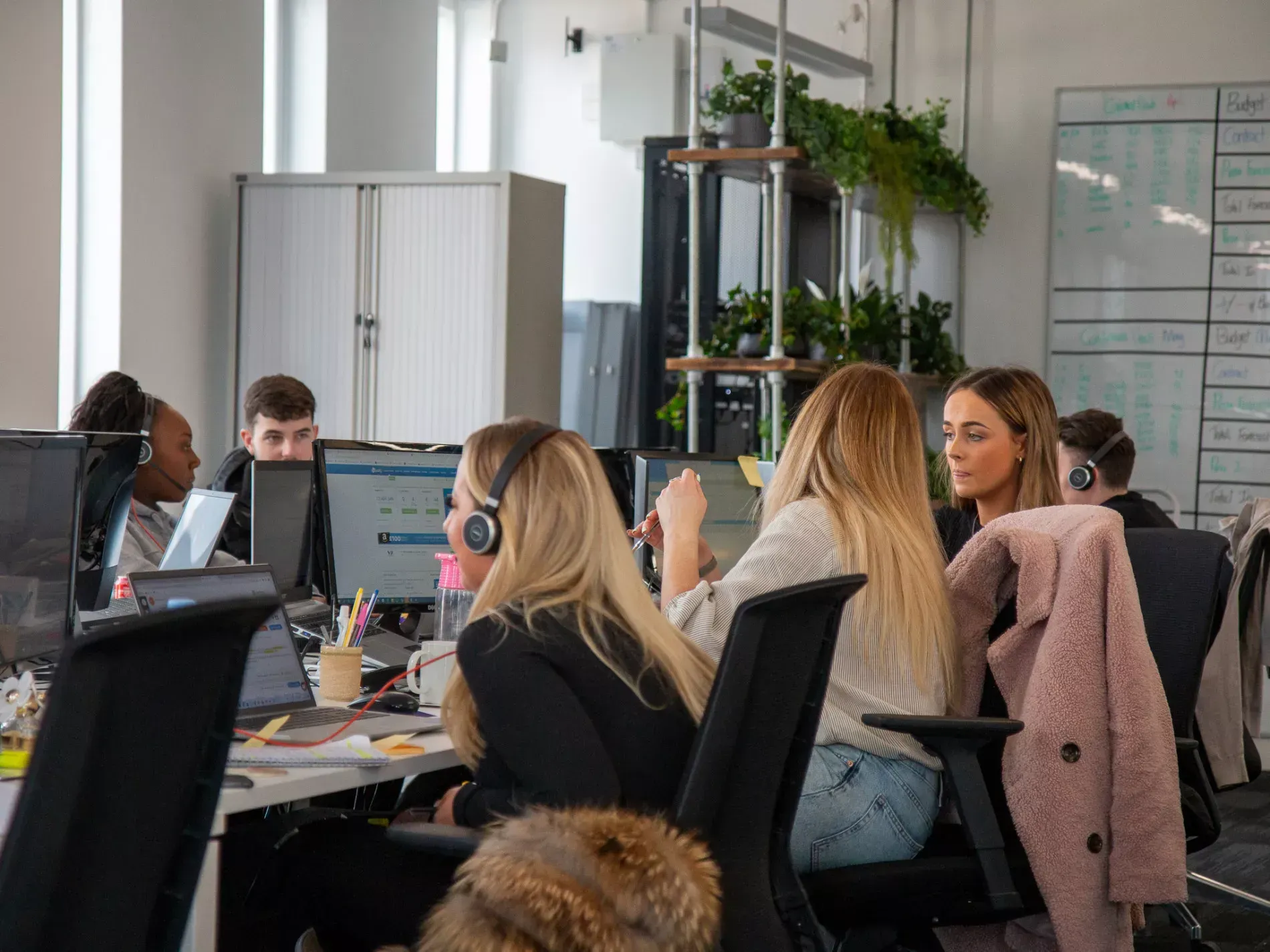 People in office setting, wearing headsets, looking at computer screens, working.