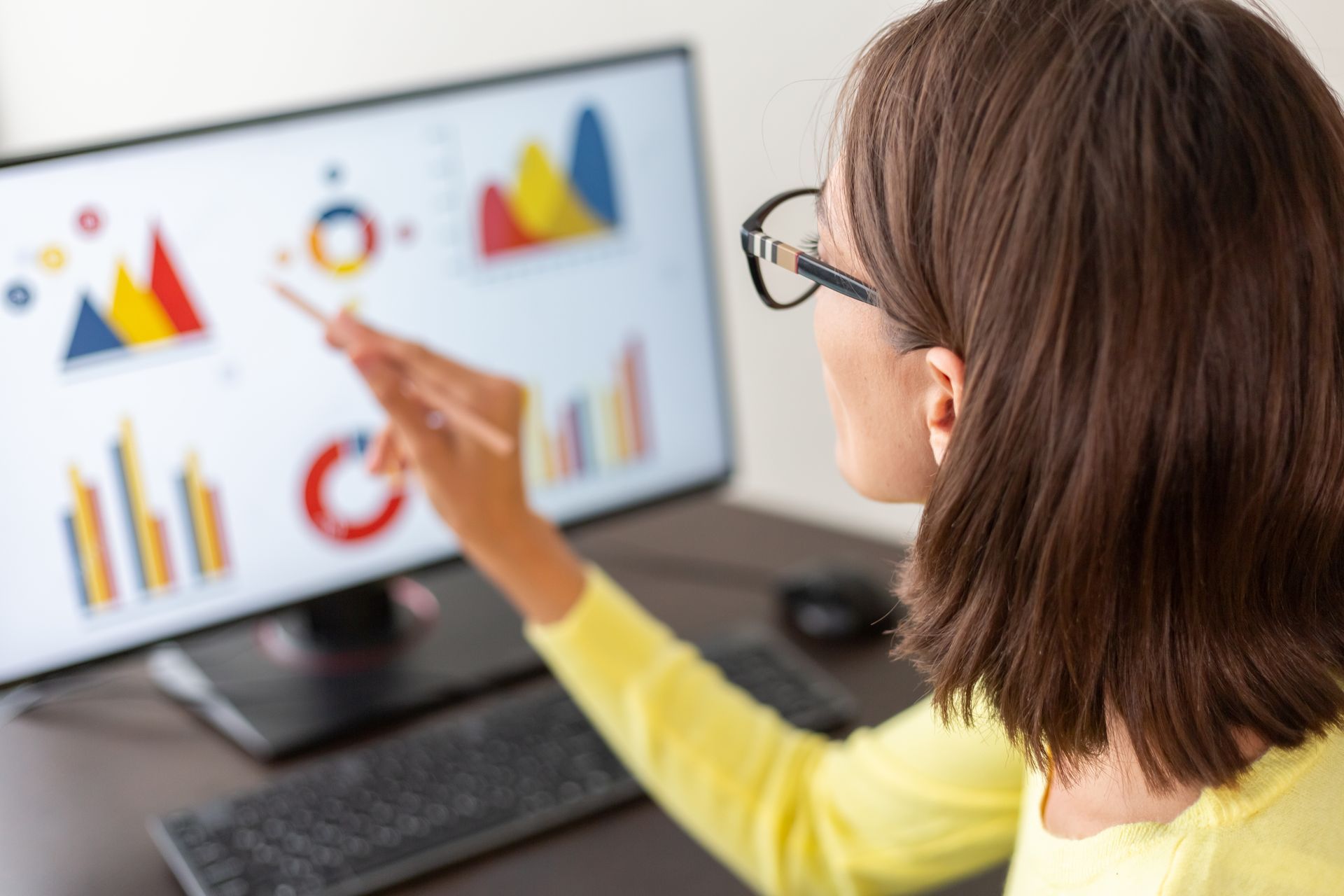 Person pointing at colorful charts on a desktop monitor in an office setting