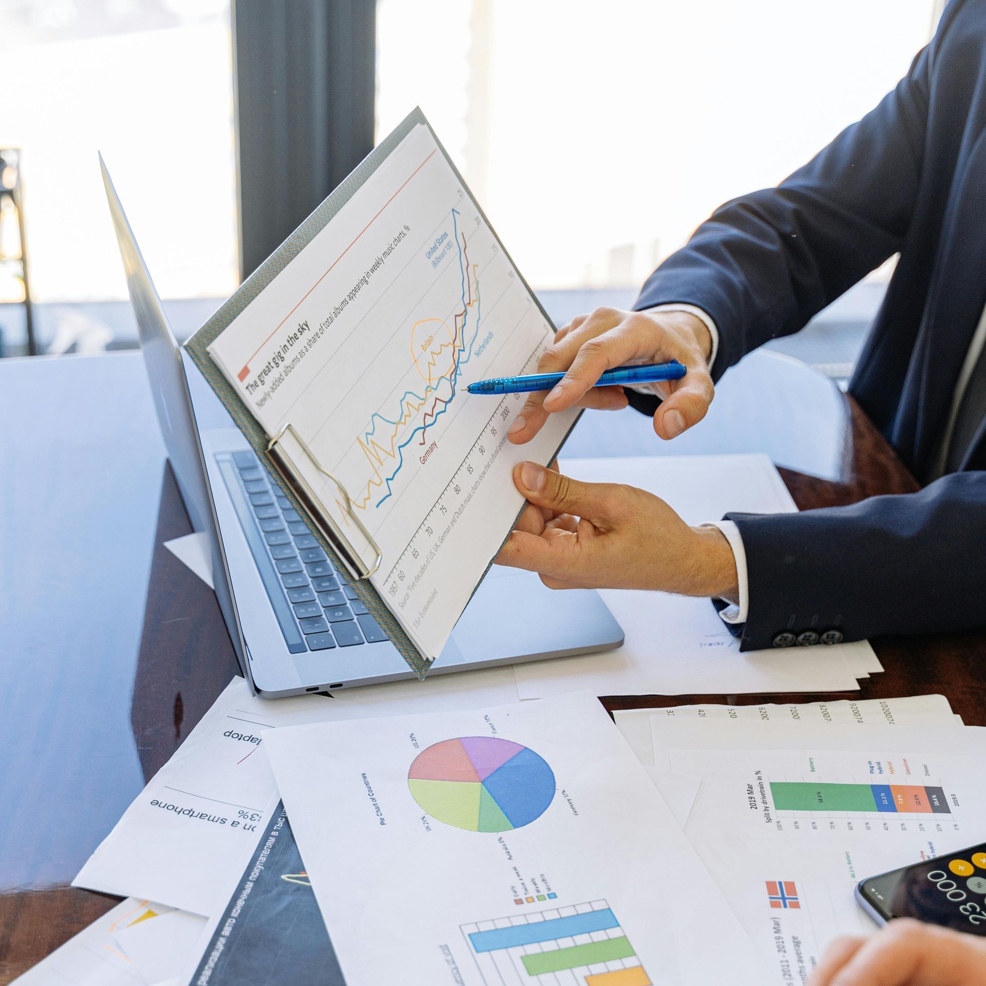 A man is pointing at a graph on a piece of paper in front of a laptop.
