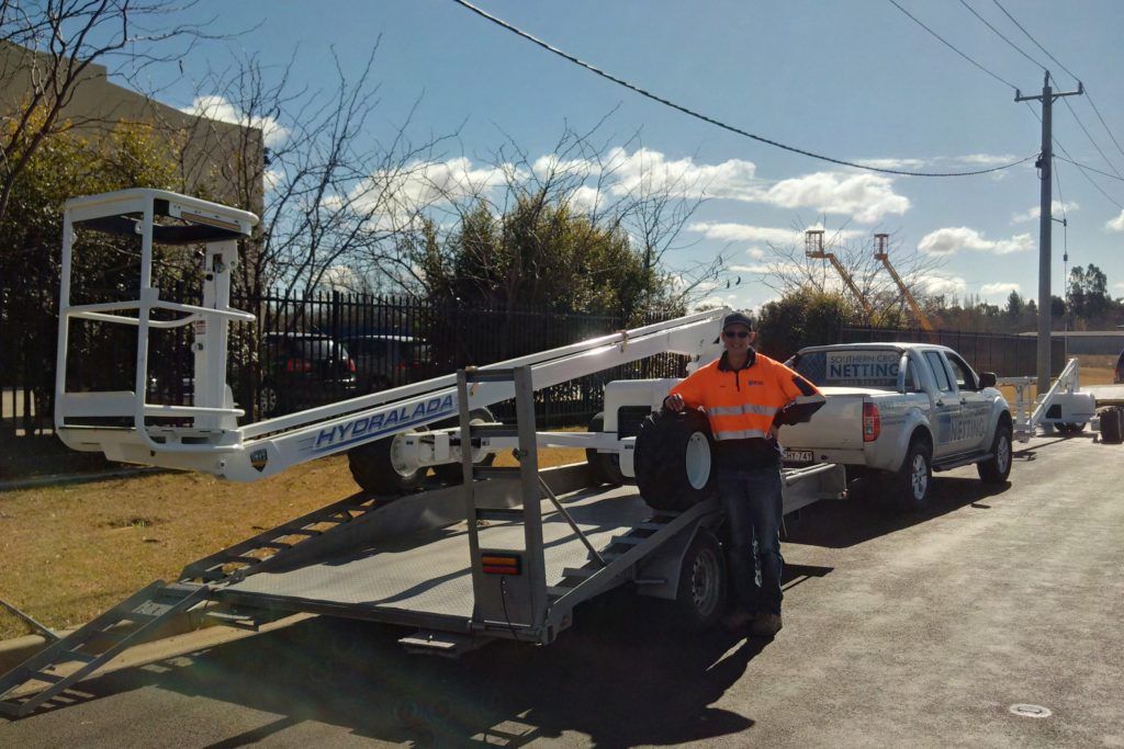 Orange boom lift with a worker elevated on a platform in an outdoor lot.