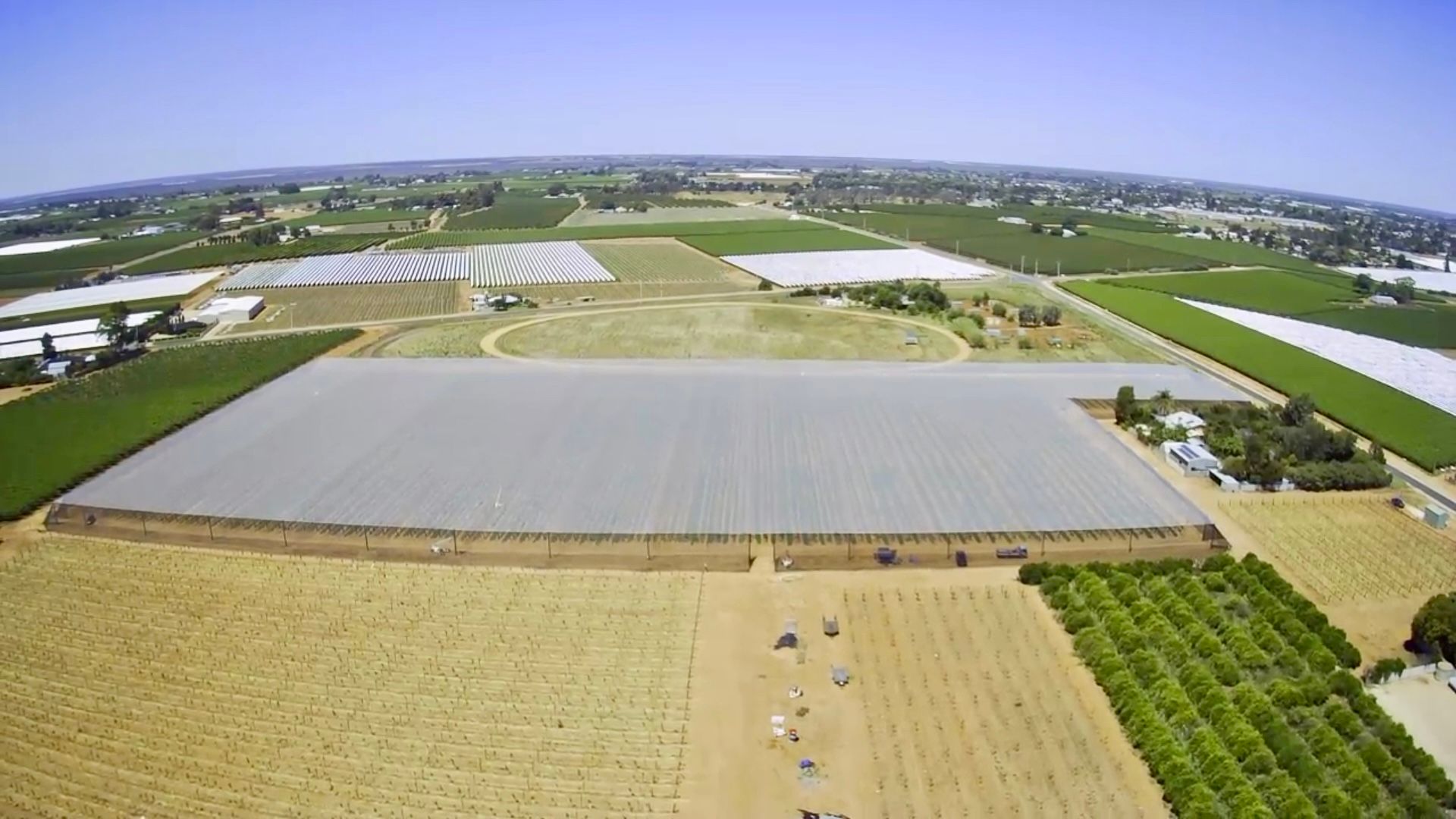 Aerial view of farm fields with large white-covered plots and green crops in a rural landscape
