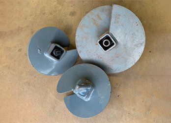 Three metal disc parts with central square mounts on a tan surface.