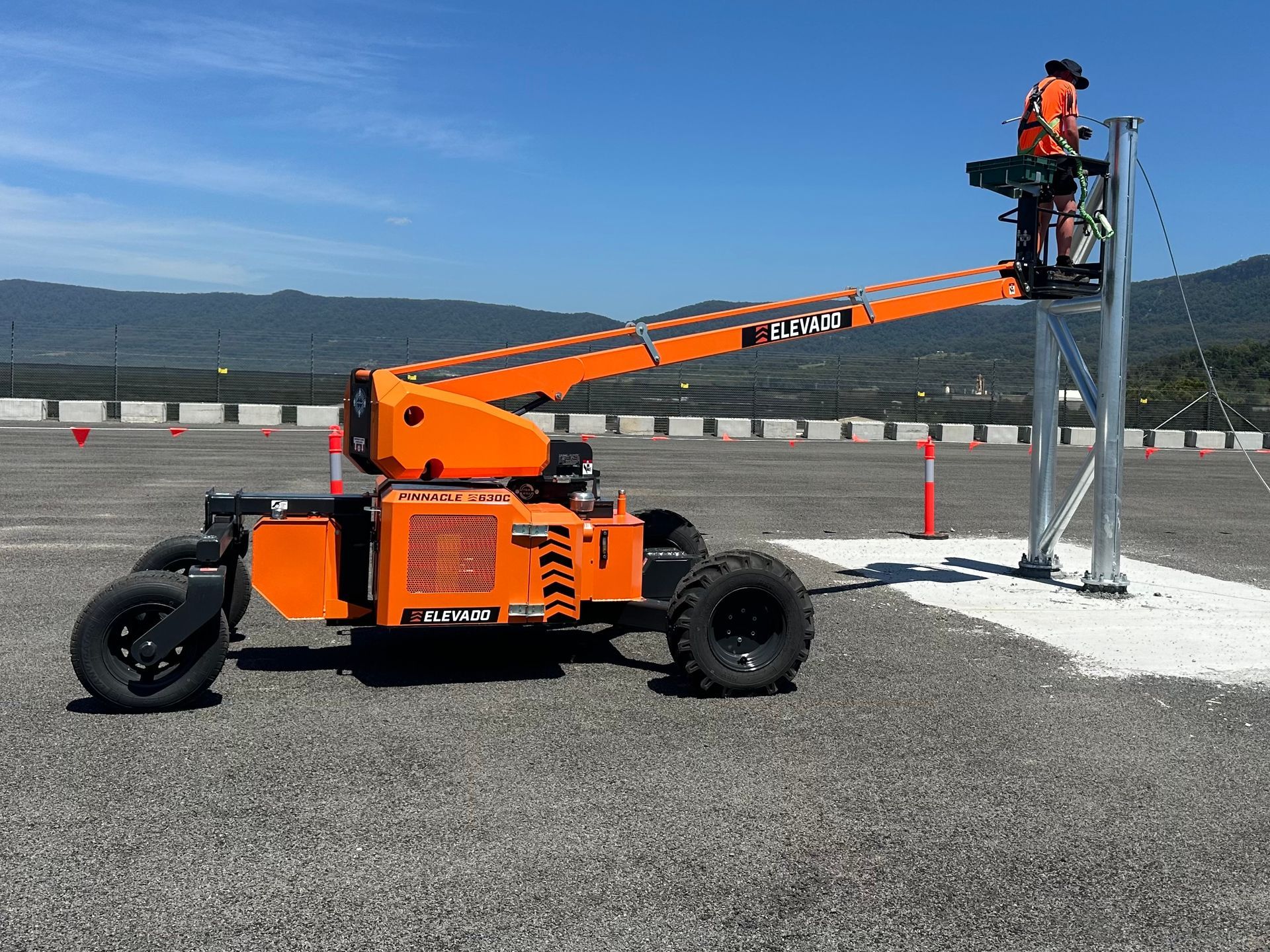 Orange boom lift with a worker elevated on a platform in an outdoor lot.
