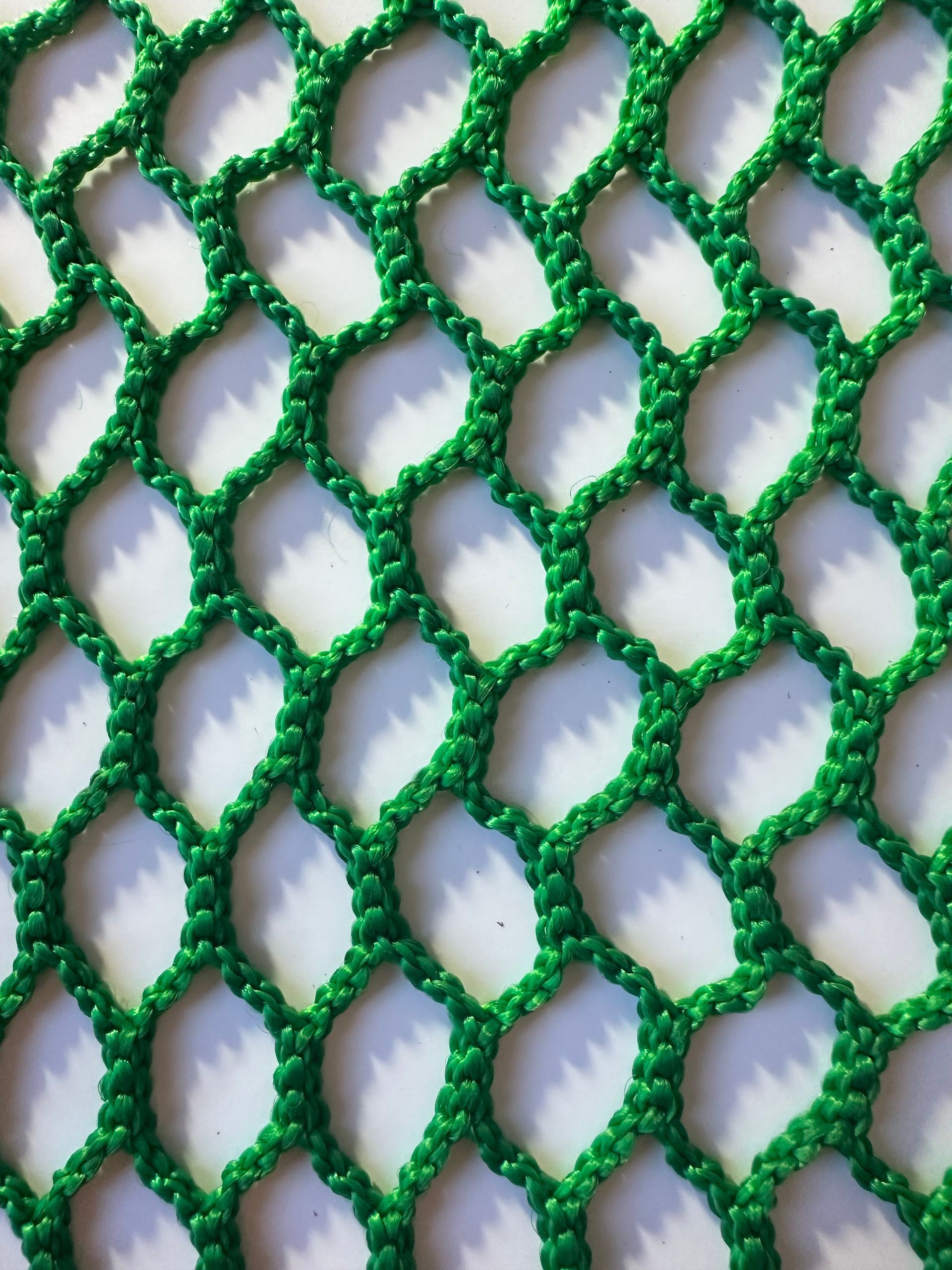 Close-up of green netting with diamond-shaped openings over a white background