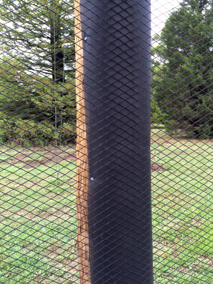 Black woven mesh wraps a utility pole in a grassy wooded area