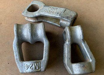 Three silver metal cable clamps arranged on a tan surface, two upright and one lying above them