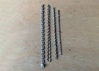 Four metal drill bits lined up on a beige surface, arranged from longest to shortest.
