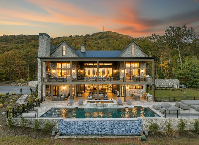 Luxury home with stone exterior, pool, and mountain backdrop at sunset.