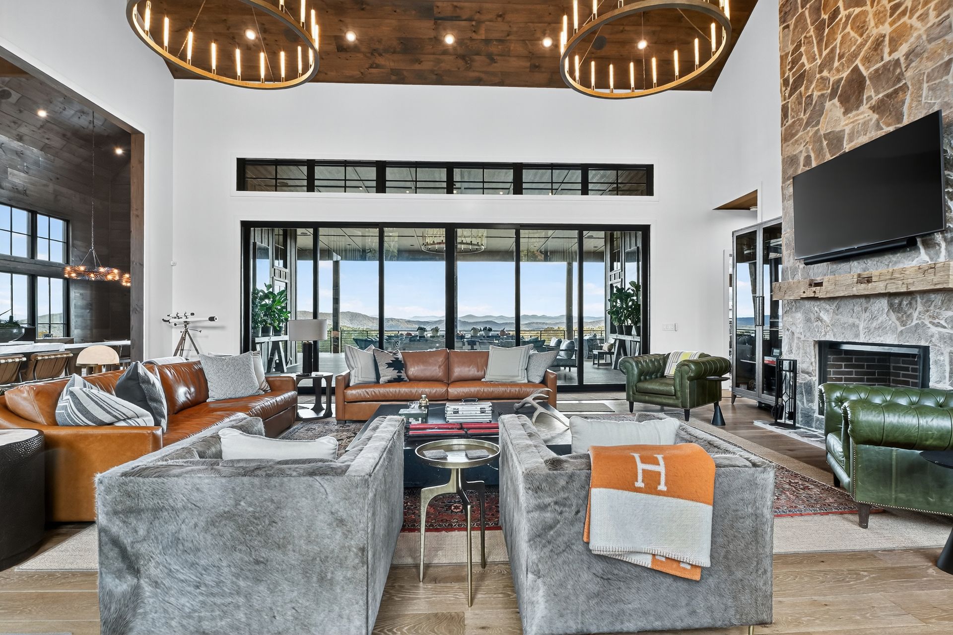 Spacious living room with large windows, fireplace, leather furniture, and chandeliers.