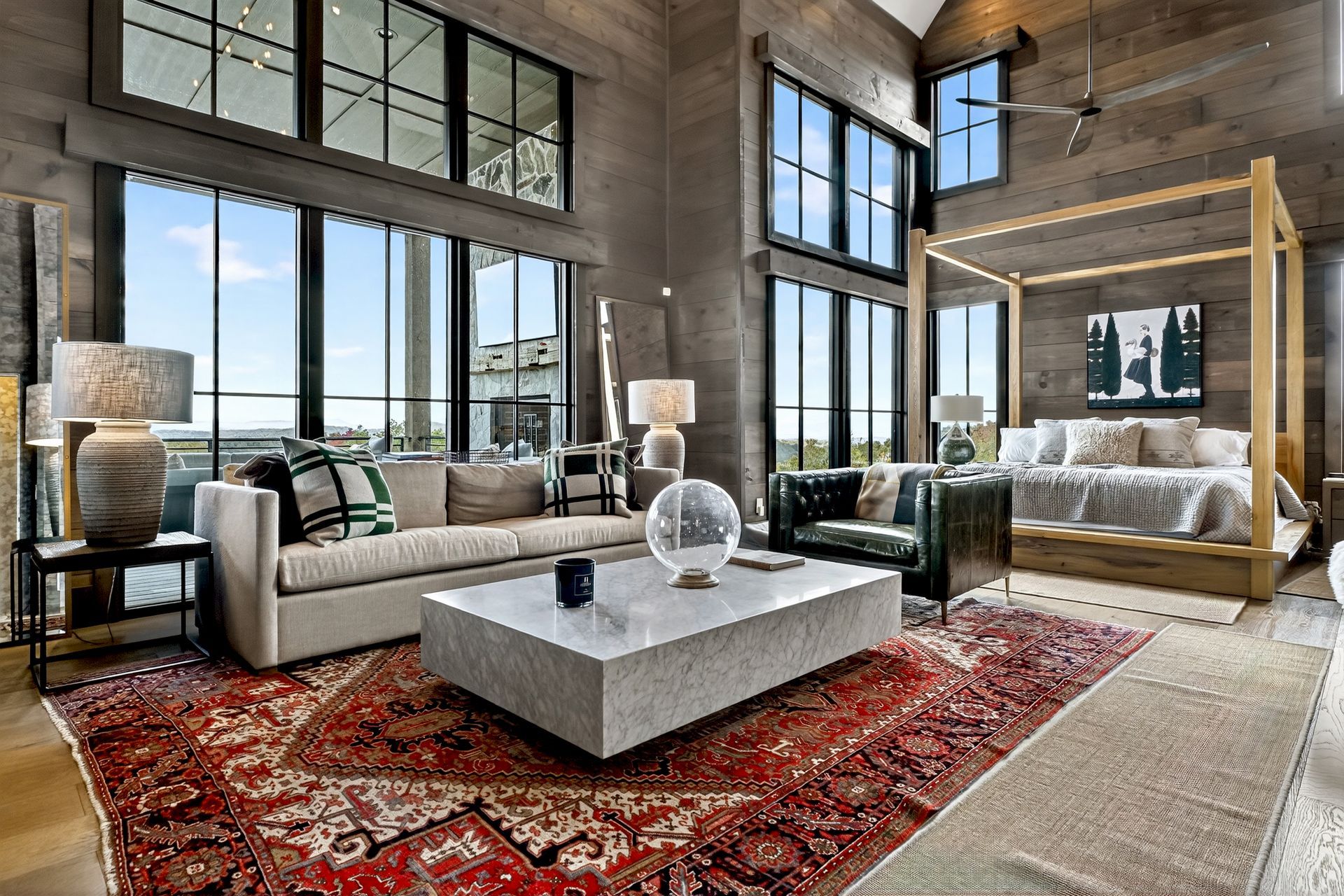 Luxurious bedroom with large windows, sofa, bed, and vibrant patterned rug.