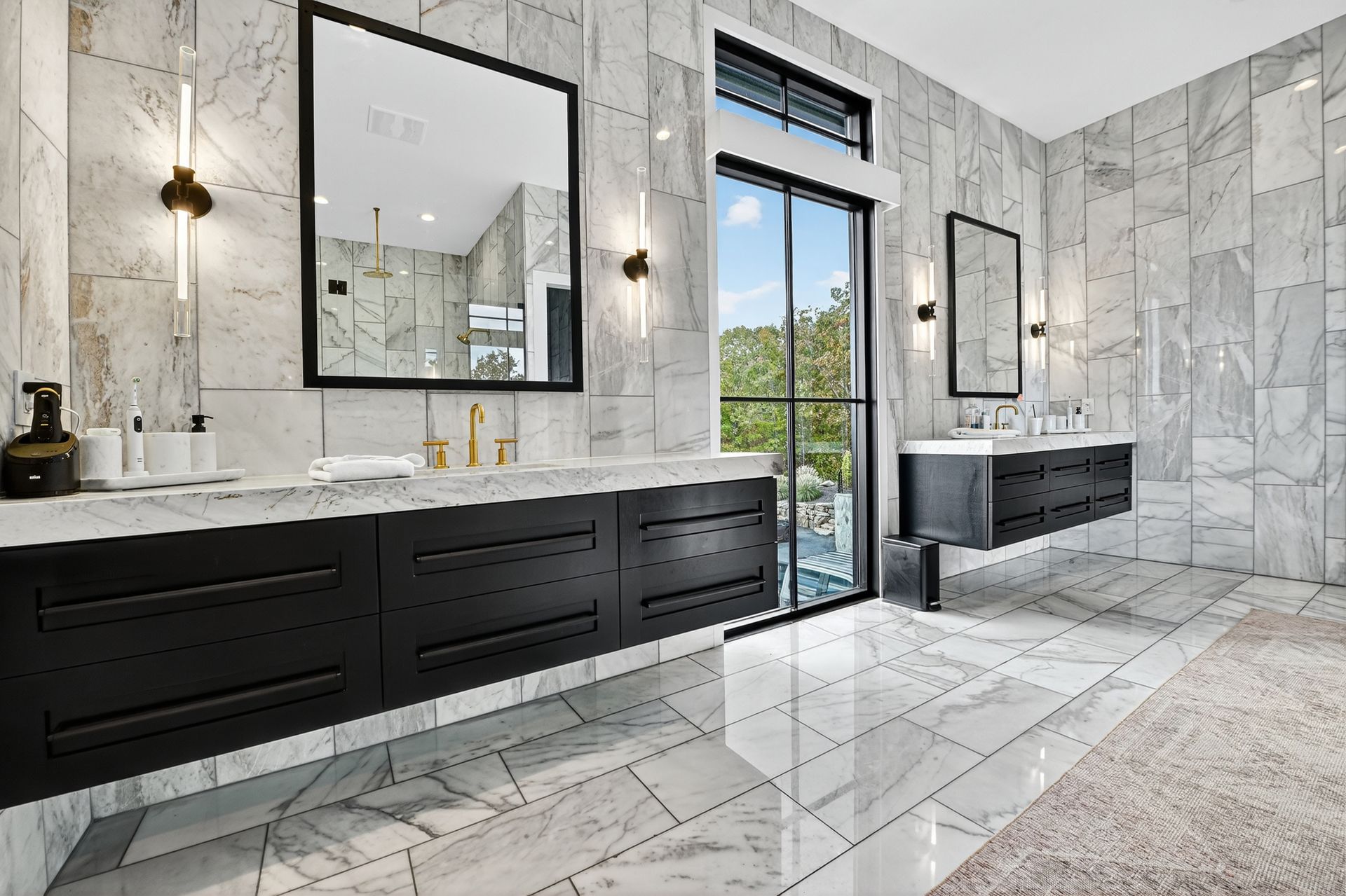 Luxurious bathroom with marble walls, black cabinets, gold fixtures, and a window overlooking a pool area.