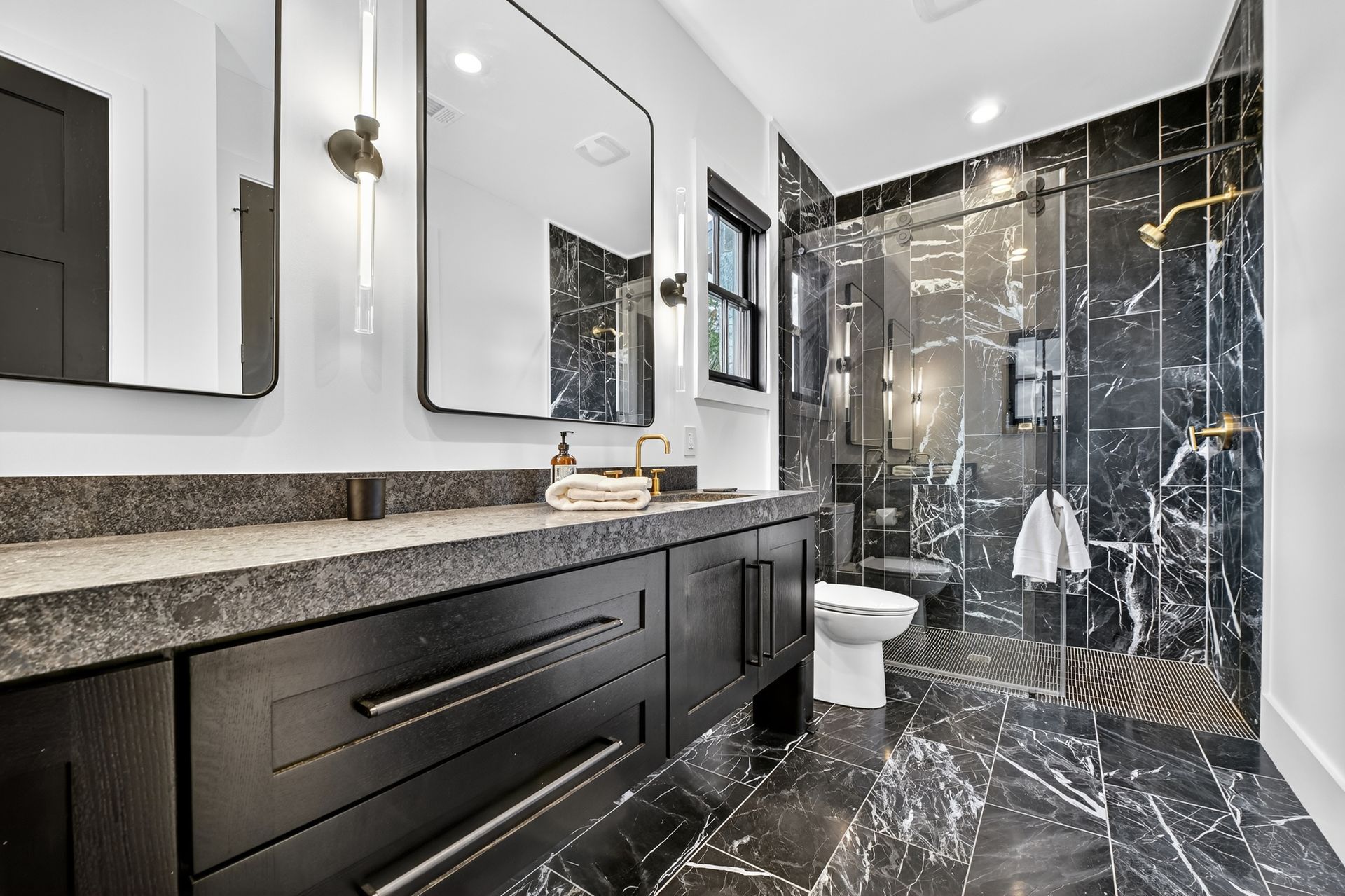 Modern bathroom with black vanity, marble-like tile, and glass shower.