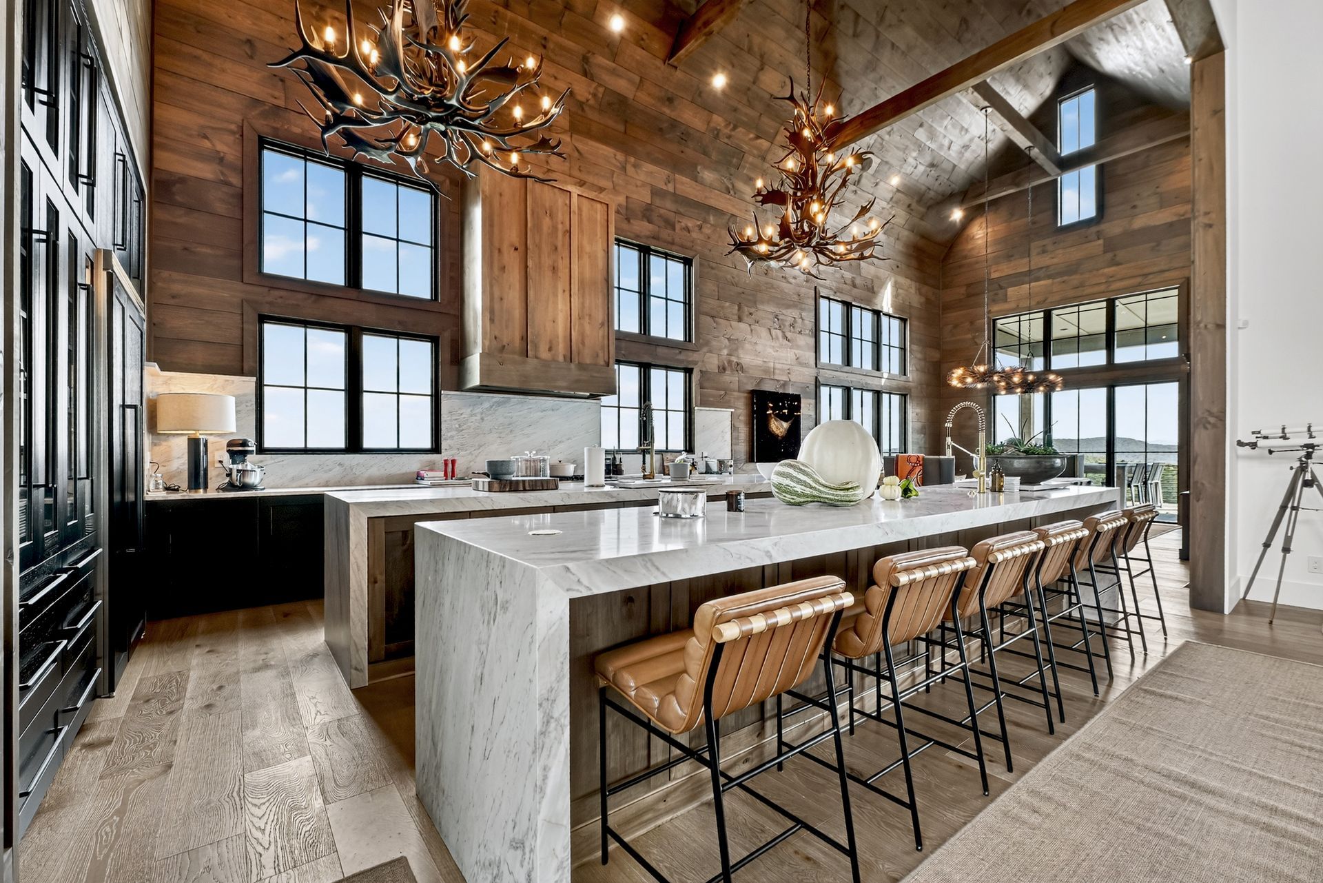 Rustic kitchen with wood paneling, large island with seating, and chandelier lighting.