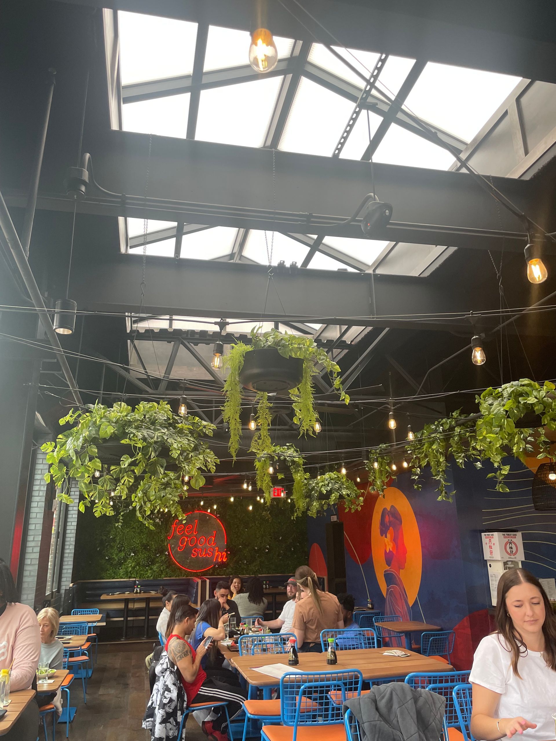 Indoor café with hanging plants, skylights, and people dining at blue tables.