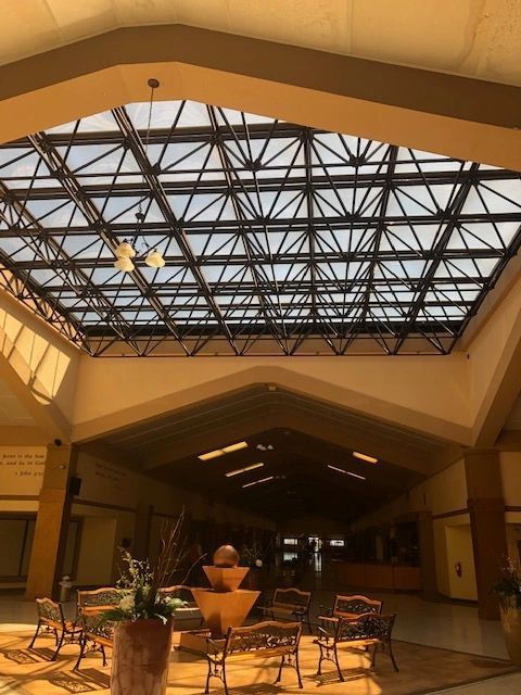 Spacious atrium with a glass roof, triangular beams, and a central fountain surrounded by chairs and tables