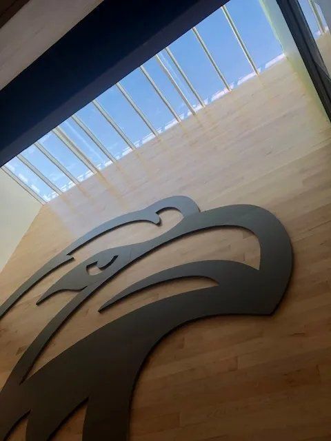 Large black eagle logo on a curved wooden wall beneath a skylight in a modern interior.