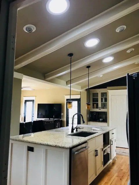 Modern kitchen with white cabinets, granite island, stainless appliances, and recessed ceiling lights.