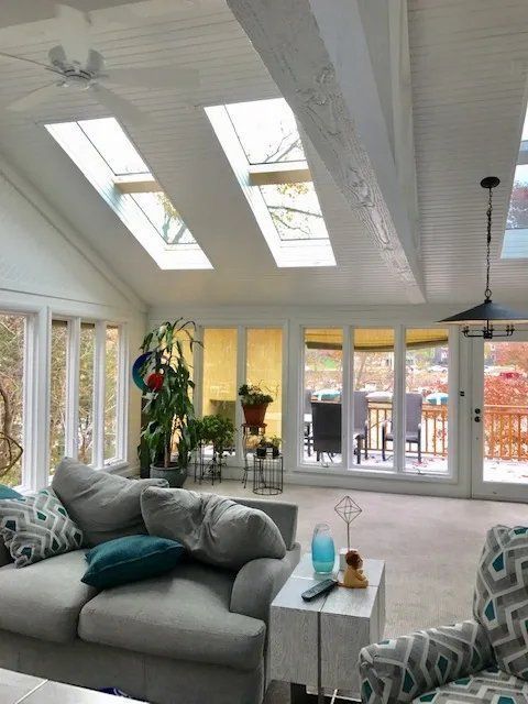 Bright sunroom with skylights, gray sectional sofa, dining area, and large windows overlooking a patio.