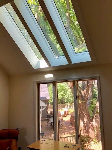 Room with slanted skylights and a sliding glass door opening to a sunlit backyard with a tree.