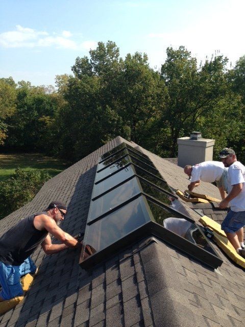 Two workers install black solar panels on a shingled rooftop on a sunny day.