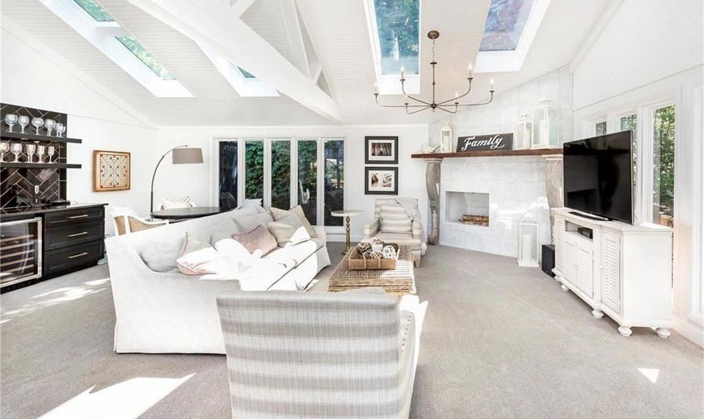 Bright modern living room with white sofas, striped chair, skylights, and TV cabinet