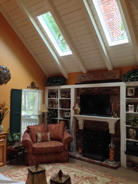 Cozy living room with vaulted ceiling, fireplace, bookshelves, and red armchair by a window