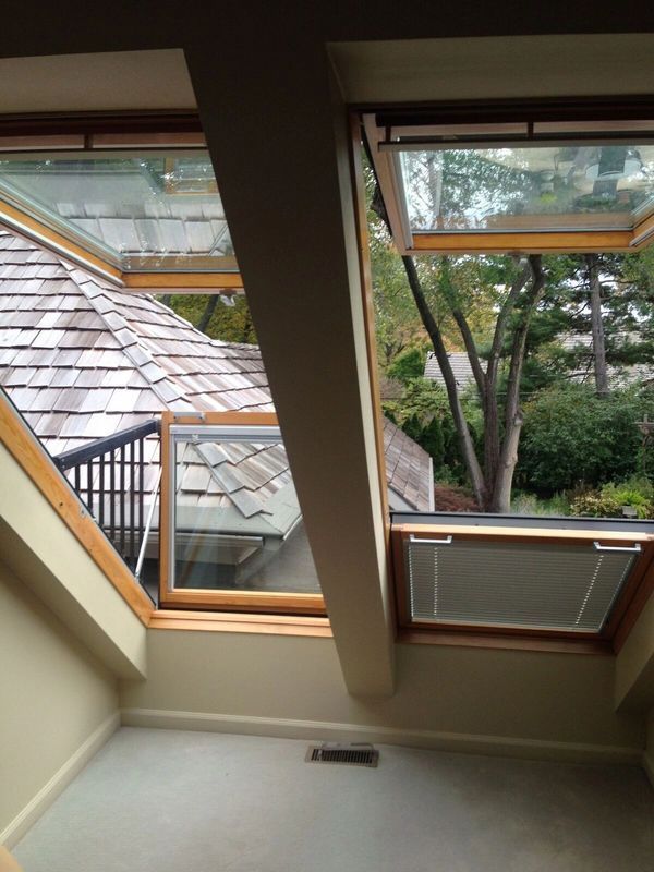 Attic window view of rooftops, trees, and neighboring houses beside a skylight and ceiling beam