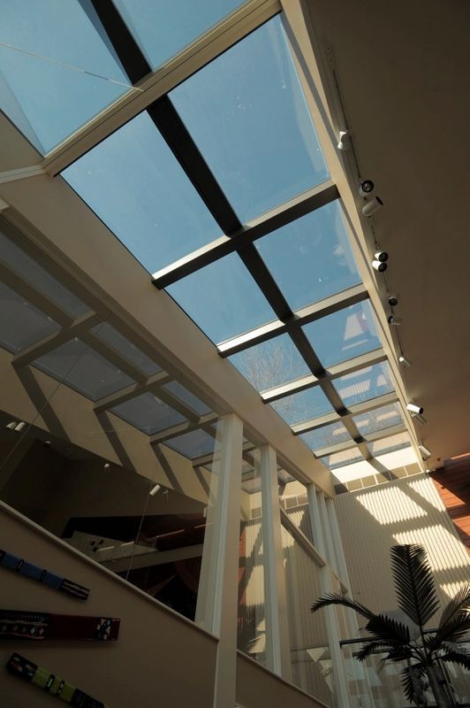 Interior atrium with glass skylight ceiling, white columns, and a potted plant in sunlight