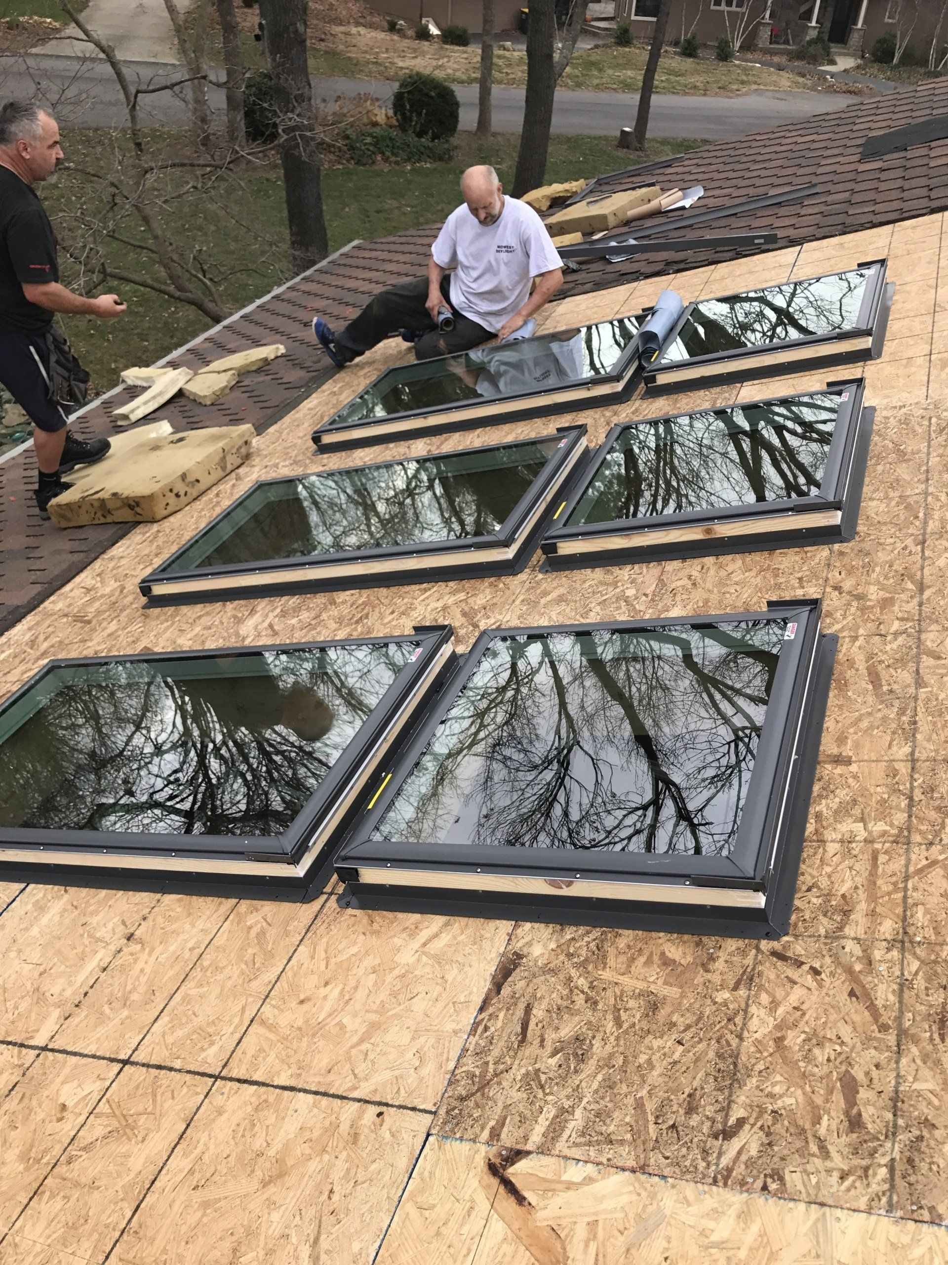 Workers installing large skylight windows on a plywood roof deck outdoors
