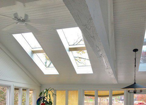 Bright sunroom ceiling with skylights, white beams, and a hanging light fixture