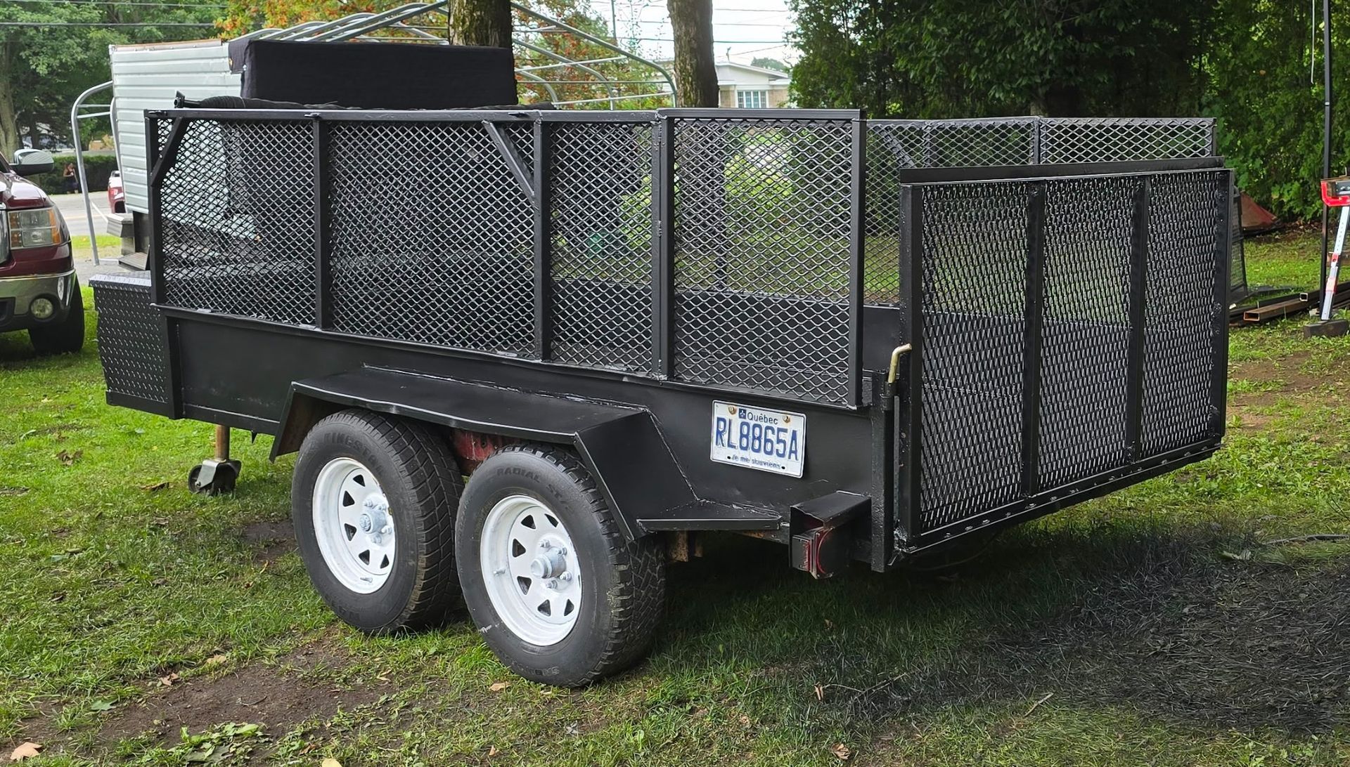 Remorque utilitaire noire avec côtés grillagés, deux roues blanches, sur herbe.