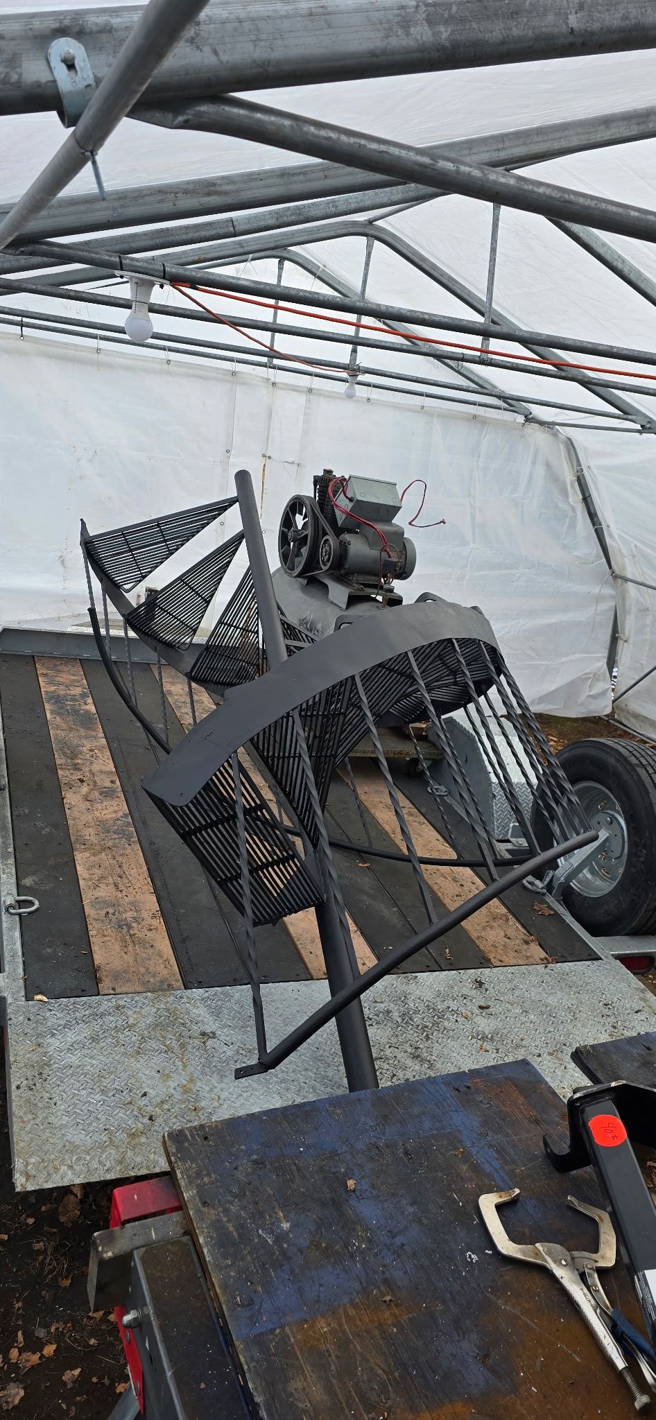 Machine agricole sur remorque sous une structure métallique. La machine est dotée d'un châssis, de roues et d'un moteur en métal.